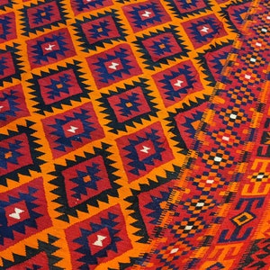 May include: A colorful rug with a geometric pattern in shades of orange, red, blue, and black. The rug has a traditional design with intricate details.