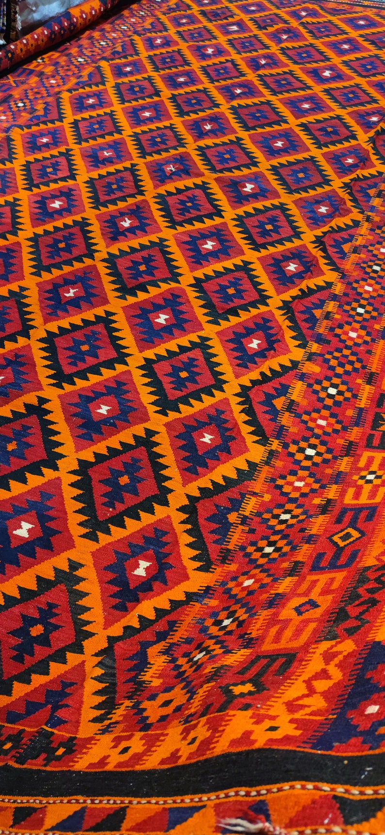 May include: A colorful rug with a geometric pattern in shades of orange, red, blue, and black. The rug has a traditional design with intricate details.