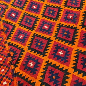 May include: A colorful rug with a geometric pattern in shades of orange, red, black, and blue. The rug has a diamond-shaped pattern with intricate details.
