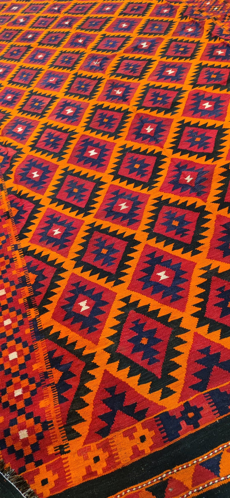 May include: A colorful rug with a geometric pattern in shades of orange, red, black, and blue. The rug has a diamond-shaped pattern with intricate details.