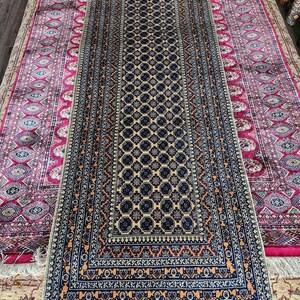 Könnte beinhalten: Ein langer, schmaler Teppich mit einem geometrischen Muster in Blautönen, Beige und Orange. Der Teppich hat einen Fransenrand und liegt auf einem beigefarbenen Teppich.