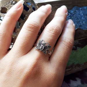 May include: A silver ring with a butterfly design made of small black stones. The ring is on a person's finger.