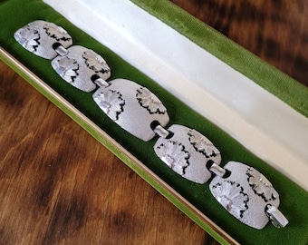 May include: A silver bracelet with a floral design. The bracelet is in a green velvet box.