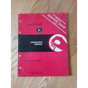 May include: A red and black John Deere Operator's Manual for 1, 2, 3, and 4-Row Row-Crops. The manual has the text "Operator's Manual" and "File this new manual". The cover also has the text "Dealer Service Shop Copy".