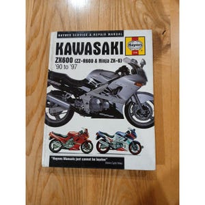 Può includere: Un manuale di servizio e riparazione Haynes per motociclette Kawasaki ZX600 (ZZ-R600 e Ninja ZX-6) dal '90 al '97. La copertina presenta una motocicletta argentata e immagini più piccole di motociclette rosse, blu e bianche. Il testo recita "Haynes Manuals just cannot be beaten."
