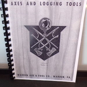 Puede incluir: Portada en blanco y negro de un catálogo de hachas y herramientas de tala. La portada presenta un bulldog mascota y un logotipo con hachas cruzadas. El texto en la portada dice "AXES AND LOGGING TOOLS" y "CATALOG Number 14" y "WARREN AXE & TOOL CO., WARREN, PA."