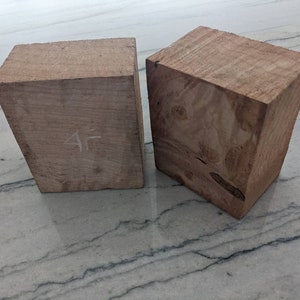 May include: Two unfinished, light brown wooden blocks. One block has the number "4F" written on it in white. The blocks are rectangular with angled sides, showcasing the natural wood grain.