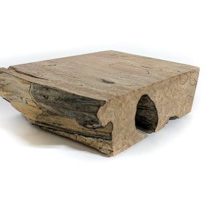 May include: A rectangular, natural wood block with a rough, textured edge and a hollowed-out section. The wood has a mix of light and dark brown tones, with visible grain and cracks. The block is set against a white background.