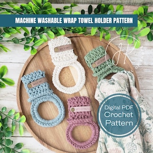 May include: Four crocheted towel holders in different colours, including beige, green, blue, and pink, with a brown leather tag that says "Jarful of Knots". The holders are displayed on a wooden surface with a floral fabric in the background. Digital PDF Crochet Pattern.