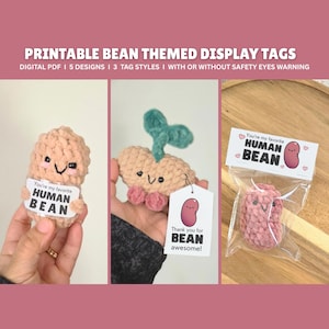 Puede incluir: Etiquetas de exhibición imprimibles con temática de frijoles. La imagen muestra tres figuras de ganchillo con forma de frijol, cada una con una cara sonriente y una etiqueta que dice "You're my favorite HUMAN BEAN" o "Thank you for BEAN awesome!"
