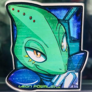 May include: A sticker depicting a green alien with orange eyes and red spots, wearing a blue and white outfit. The sticker has the text "LEON POWALSKI" in white and green.