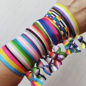 May include: A stack of colourful rainbow patterned hair ties with different pride flags, including the transgender, lesbian, gay, bisexual, and pansexual flags.