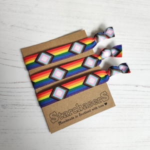 May include: Set of four rainbow patterned hair ties with a white and pink diamond design. The hair ties are packaged on a brown card with the text "Starchasers Handmade in Scotland with love".