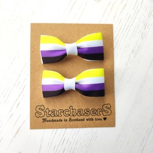 May include: Two yellow, white, purple and black bow clips on a brown card with the text "StarchaserS Handmade in Scotland with love".