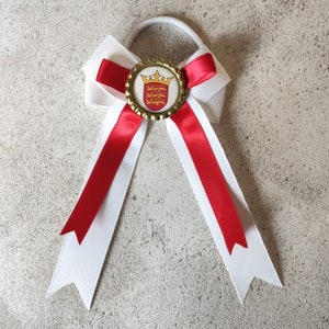 May include: A white and red bow with a gold and red crown emblem on a white background. The bow is tied with a white elastic band.