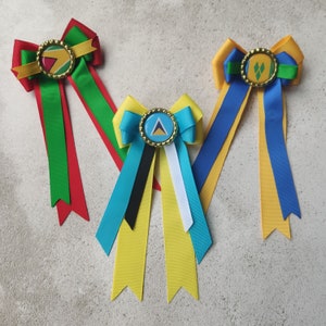 May include: Three handmade hair bows with different colored ribbons and a small button with a country flag design in the center. The bows are yellow, blue, and green with red, white, and black ribbons.