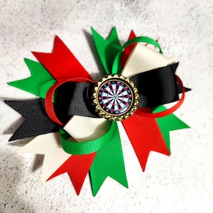 May include: A decorative bow made with red, black, green, and cream ribbons. The bow has a dartboard design in the centre, set within a gold-coloured bottle cap. This handcrafted item is suitable for various events and celebrations.