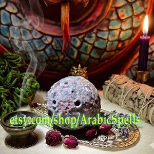 May include: A textured, cratered, spherical object resembling a moon, resting on an ornate silver tray with dried red rosebuds and lavender. The text "etsy.com/shop/ArabicSpells" is overlaid in yellow. A purple candle and incense smoke are visible.
