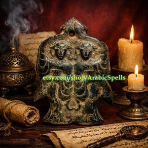 May include: A dark green, weathered, carved stone amulet featuring two faces. The amulet is displayed with lit candles, scrolls, and an incense burner. The Etsy shop name "ArabicSpells" is visible on the amulet.