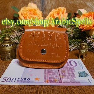 May include: A tan leather pouch with embossed symbols and text, fastened with a press stud. The pouch is placed on a 500 Euro note. The text "etsy.com/shop/ArabicSpells" is visible.