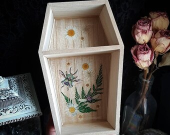 May include: A wooden box shaped like a coffin with a floral and insect design. The box has two compartments and is painted with a light wood stain.