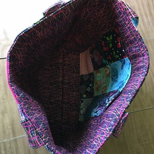 Peut inclure: L'int&eacute;rieur d'un sac fourre-tout noir et rose avec une doublure en patchwork. La doublure est faite de diff&eacute;rents tissus avec divers motifs, notamment des motifs floraux, g&eacute;om&eacute;triques et abstraits.