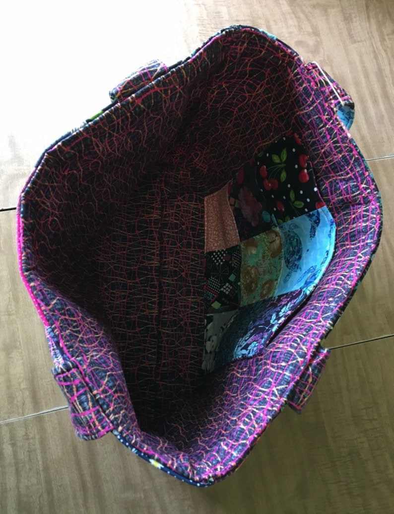 Peut inclure: L'int&eacute;rieur d'un sac fourre-tout noir et rose avec une doublure en patchwork. La doublure est faite de diff&eacute;rents tissus avec divers motifs, notamment des motifs floraux, g&eacute;om&eacute;triques et abstraits.