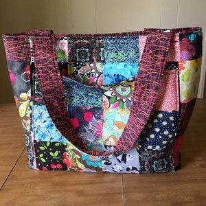 Peut inclure: Un sac fourre-tout en patchwork avec une vari&eacute;t&eacute; de tissus color&eacute;s. Le sac a deux longues lani&egrave;res et une poche sur le devant.