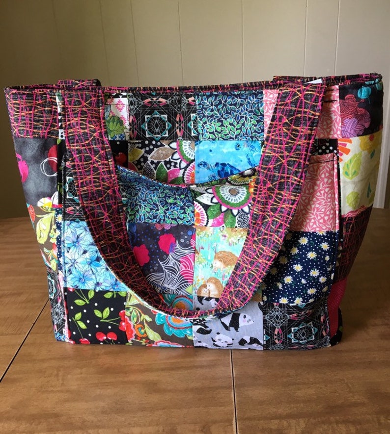 Peut inclure: Un sac fourre-tout en patchwork avec une vari&eacute;t&eacute; de tissus color&eacute;s. Le sac a deux longues lani&egrave;res et une poche sur le devant.