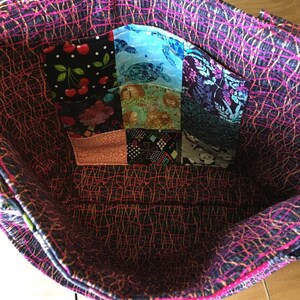 Peut inclure: L'int&eacute;rieur d'un sac fourre-tout noir et rose avec une poche en patchwork faite de diff&eacute;rents tissus color&eacute;s. La poche est compos&eacute;e de 9 carr&eacute;s de tissu avec diff&eacute;rents motifs, dont des cerises, des tortues et des fleurs.