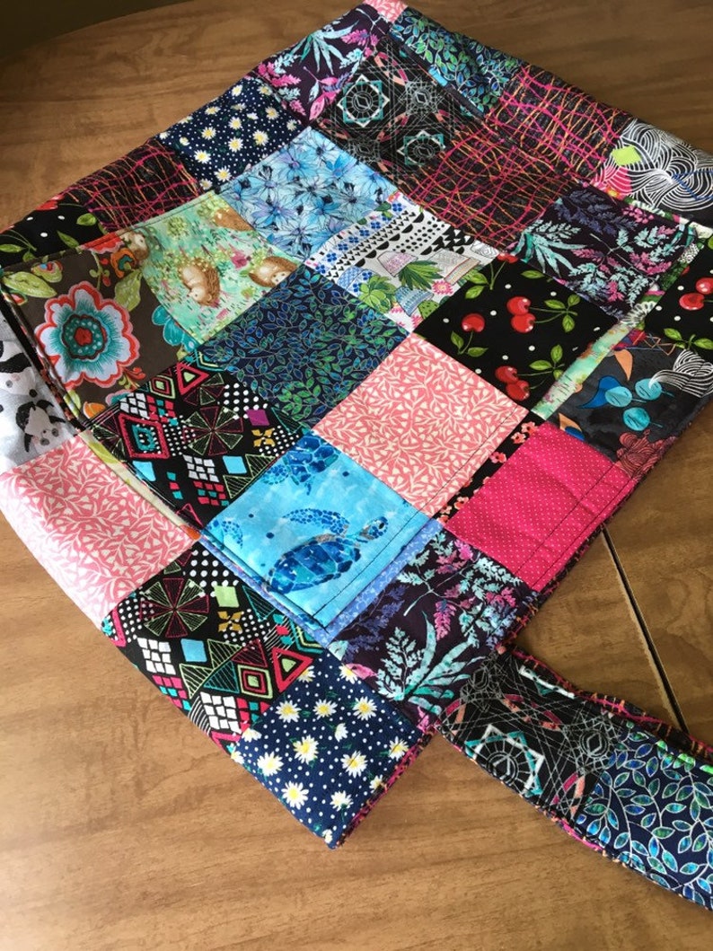 Peut inclure: Un sac fourre-tout en patchwork avec une vari&eacute;t&eacute; de tissus color&eacute;s. Le sac a un grand compartiment principal et une seule poign&eacute;e.