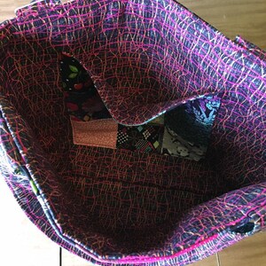 Peut inclure: L'int&eacute;rieur d'un sac cabas rose et noir avec un motif patchwork. Le sac est doubl&eacute; d'un tissu noir et blanc avec un motif rose et or.