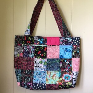 Peut inclure: Un sac fourre-tout en patchwork avec une vari&eacute;t&eacute; de tissus color&eacute;s. Le sac a une palette de couleurs noire, rose et bleue et pr&eacute;sente une vari&eacute;t&eacute; de motifs, notamment des imprim&eacute;s floraux, g&eacute;om&eacute;triques et animaliers.
