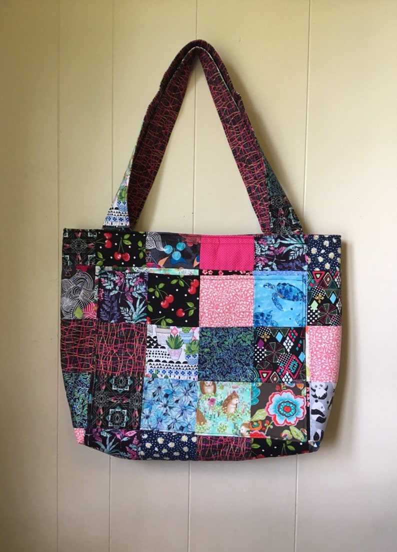 Peut inclure: Un sac fourre-tout en patchwork avec une vari&eacute;t&eacute; de tissus color&eacute;s. Le sac a une palette de couleurs noire, rose et bleue et pr&eacute;sente une vari&eacute;t&eacute; de motifs, notamment des imprim&eacute;s floraux, g&eacute;om&eacute;triques et animaliers.