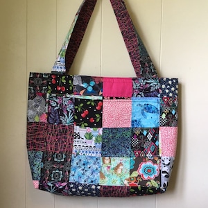 Peut inclure: Un sac fourre-tout en patchwork avec une vari&eacute;t&eacute; de tissus color&eacute;s. Le sac a une doublure rose et deux longues anses. Les motifs des tissus comprennent des cerises, des fleurs, des motifs g&eacute;om&eacute;triques et des animaux.