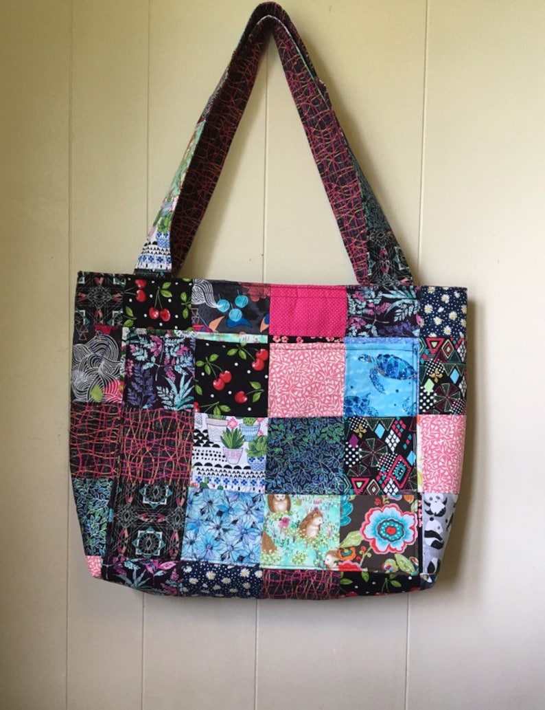 Peut inclure: Un sac fourre-tout en patchwork avec une vari&eacute;t&eacute; de tissus color&eacute;s. Le sac a une doublure rose et deux longues anses. Les motifs des tissus comprennent des cerises, des fleurs, des motifs g&eacute;om&eacute;triques et des animaux.