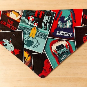 May include: A triangular fabric pet bandana featuring a collage of horror movie posters including The Exorcist, IT with Pennywise holding balloons, Annabelle, and The Lost Boys. The print displays vibrant red, black, and teal colors.