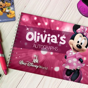 Può includere: Un libro di autografi rosa con uno sfondo scintillante e un'immagine di Minnie Mouse. Il libro dice "Olivia's Autographs" e "Walt Disney World".