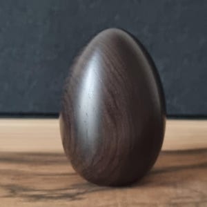 以下が含まれることがあります： 滑らかで光沢のある濃い茶色の木製卵。卵は木製の表面に立っており、背景は暗いです。木の木目が卵の表面に見えます。卵の高さは約8cmです。