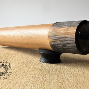 May include: A wooden kaleidoscope with a black lens and a black base. The kaleidoscope is made of two different types of wood, one light and one dark. The kaleidoscope is labeled "Armando Perri Wooden Objects".