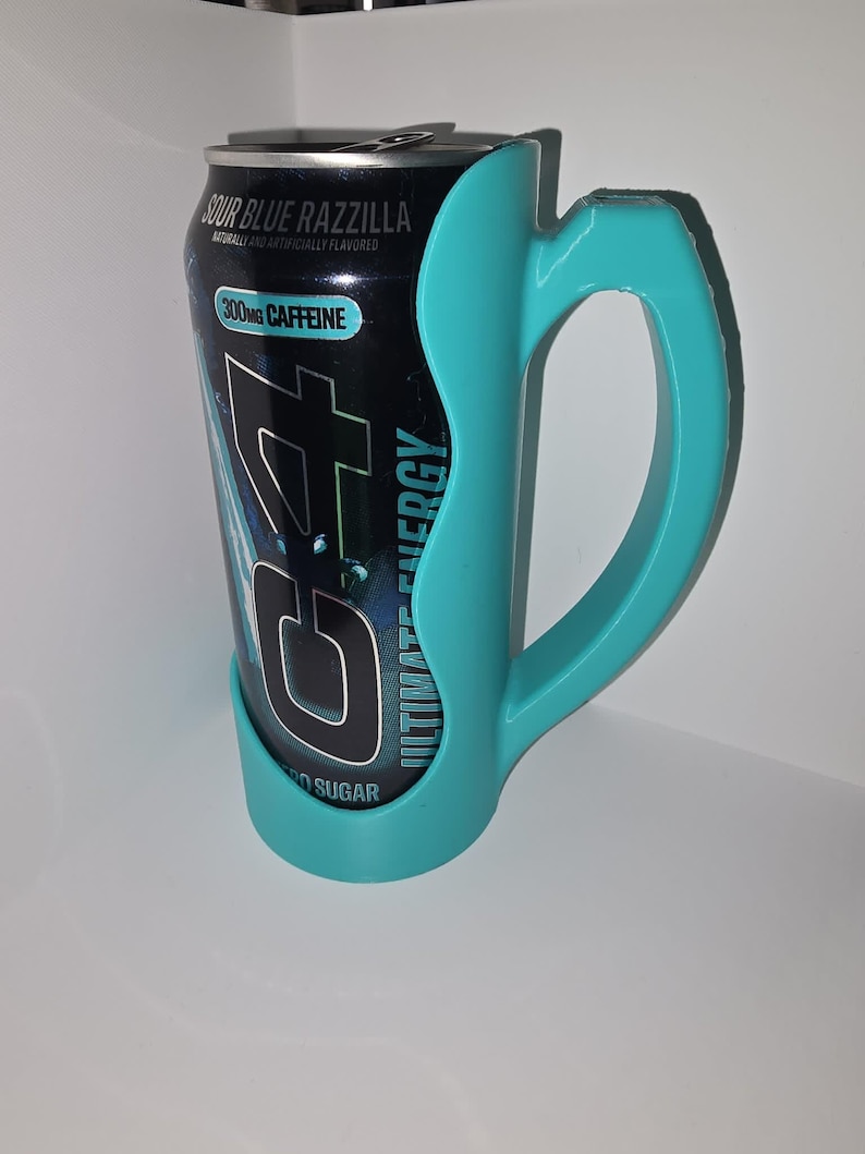 May include: A black energy drink can with the text "Sour Blue Razzilla" and "300mg Caffeine" is held by a teal-colored handle. The can is labeled "Ultimate Energy" and "No Sugar".