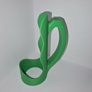 May include: A bright green, abstract-shaped object with a curved handle and a circular base. The object appears to be made of a solid material, possibly plastic or resin, and is designed with smooth, flowing lines. The object is positioned against a white background.