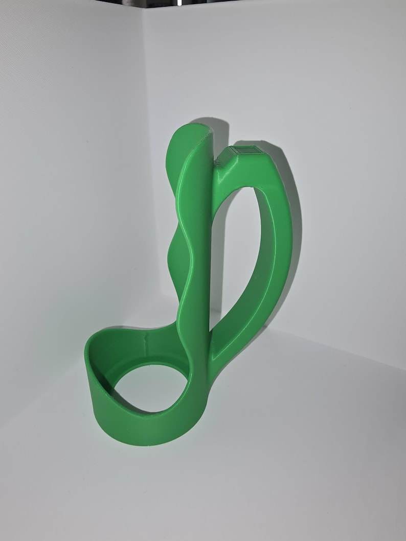 May include: A bright green, abstract-shaped object with a curved handle and a circular base. The object appears to be made of a solid material, possibly plastic or resin, and is designed with smooth, flowing lines. The object is positioned against a white background.