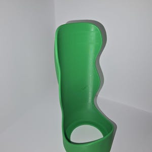 May include: A bright green, 3D-printed wrist brace. The brace has a curved design with a circular opening at the base and a contoured shape to support the wrist and forearm. The brace is made of a solid, smooth material.