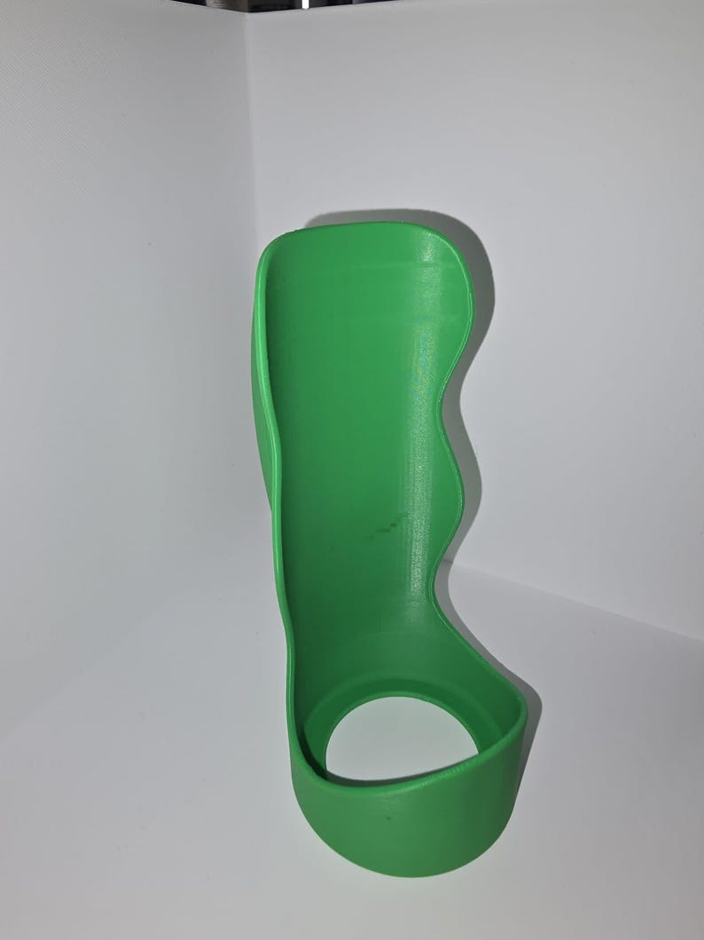 May include: A bright green, 3D-printed wrist brace. The brace has a curved design with a circular opening at the base and a contoured shape to support the wrist and forearm. The brace is made of a solid, smooth material.