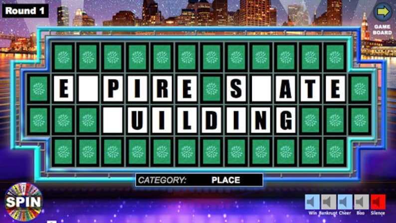 May include: A Wheel of Fortune game board with the phrase "Empire State Building" partially filled in. The category is "Place".