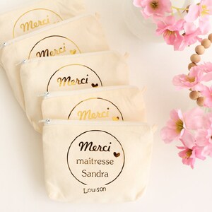 May include: Five beige zippered pouches with gold lettering that says "Merci" and a small heart. The bottom pouch has the additional text "maitresse Sandra Louison".