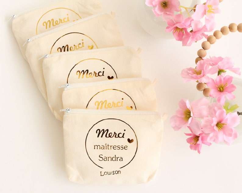 May include: Five beige zippered pouches with gold lettering that says "Merci" and a small heart. The bottom pouch has the additional text "maitresse Sandra Louison".