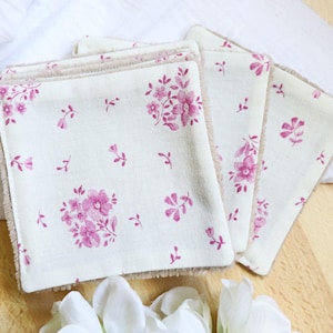 Può includere: Quattro dischetti struccanti in cotone bianco con un motivo floreale rosa e un bordo in camoscio marrone.