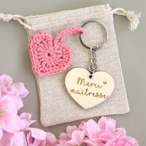 May include: Pink crocheted heart keychain with a wooden heart charm that says "Merci maitresse" in French. The keychain is in a small burlap bag.